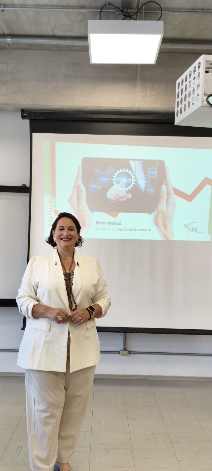 Cristiane Mayworm Montes durante uma palestra diante de uma apresentação projetada.